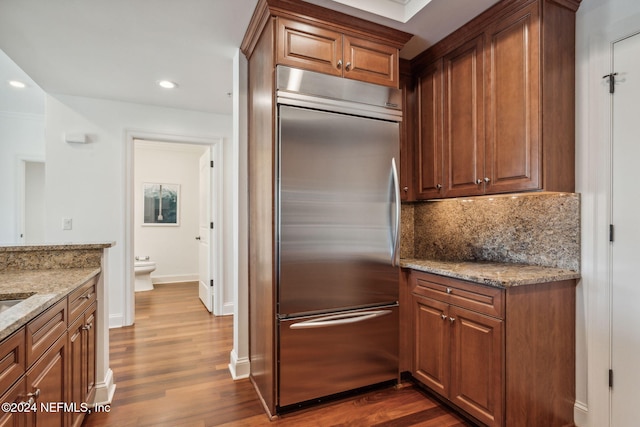 kitchen featuring dark hardwood / wood-style flooring, light stone counters, stainless steel built in fridge, and decorative backsplash