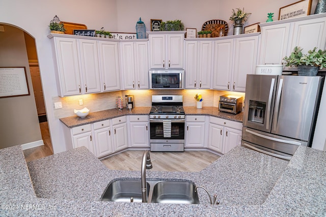 1854 W Cobblestone Ln, Saint Augustine, FL 32092 - kitchen featuring appliances with stainless steel finishes, a sink, arched walkways, light wood finished floors, and backsplash