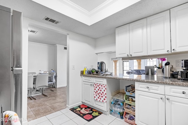 kitchen with a textured ceiling, stone countertops, white cabinetry, and ornamental molding