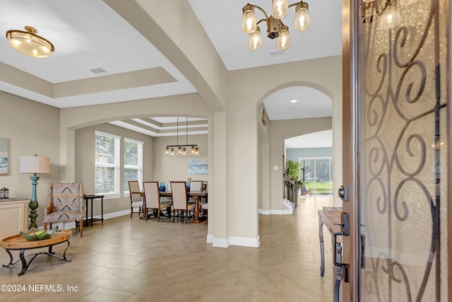 tiled entrance foyer with a notable chandelier and a tray ceiling