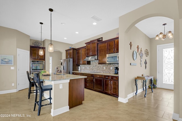 kitchen featuring a breakfast bar, sink, an island with sink, appliances with stainless steel finishes, and decorative light fixtures