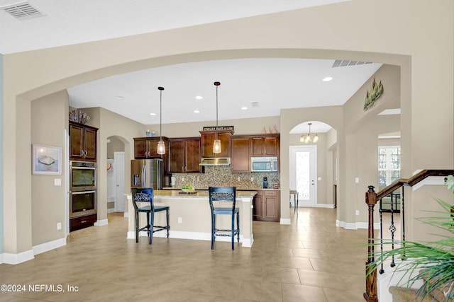 kitchen with a kitchen bar, decorative backsplash, stainless steel appliances, decorative light fixtures, and a center island