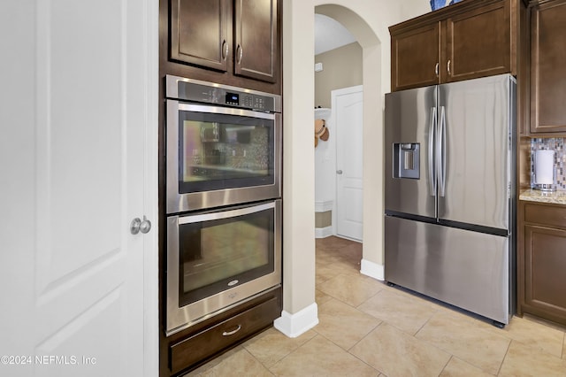 kitchen featuring dark brown cabinets, light stone counters, light tile patterned floors, and appliances with stainless steel finishes