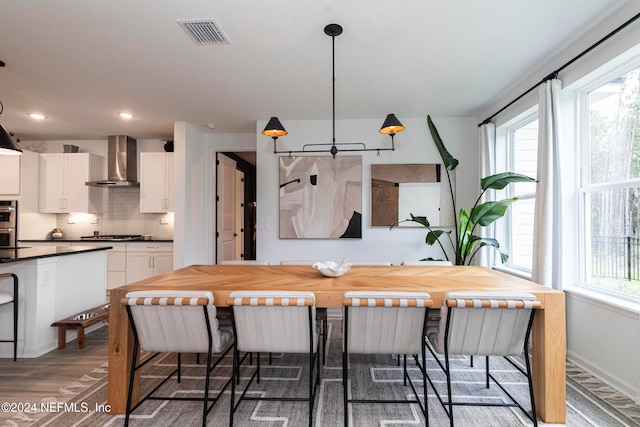 kitchen featuring wall chimney exhaust hood, pendant lighting, wood-type flooring, a breakfast bar area, and white cabinets