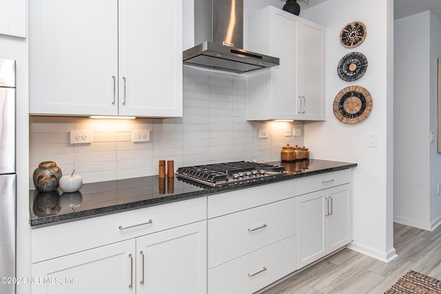 kitchen featuring white cabinets, light wood-type flooring, wall chimney exhaust hood, and dark stone countertops