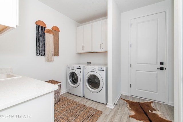 laundry area featuring cabinets, washing machine and dryer, and light hardwood / wood-style flooring