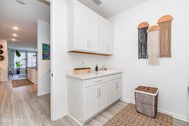 bar featuring white cabinets, light hardwood / wood-style flooring, and sink