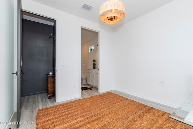 unfurnished bedroom featuring ensuite bathroom and light hardwood / wood-style flooring