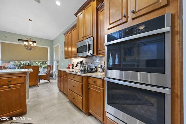 kitchen with light stone countertops, appliances with stainless steel finishes, backsplash, a chandelier, and light tile patterned flooring