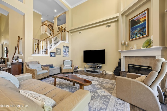 living room with hardwood / wood-style flooring, crown molding, a high ceiling, and a tiled fireplace