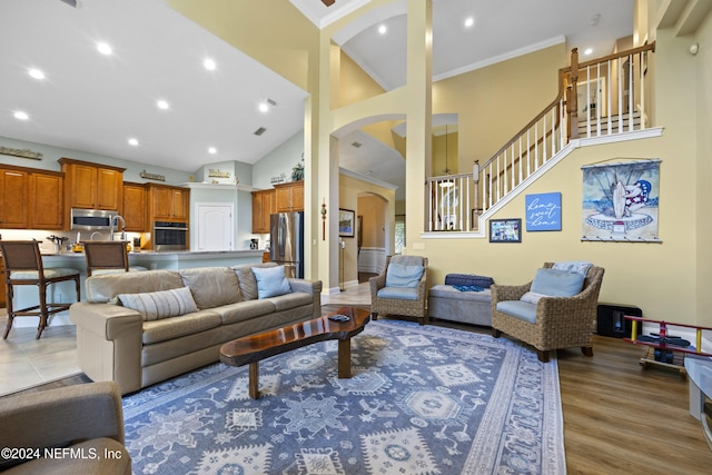 living room with light hardwood / wood-style floors, high vaulted ceiling, and ornamental molding