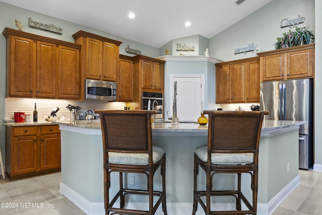 kitchen with light stone countertops, a breakfast bar, stainless steel appliances, lofted ceiling, and an island with sink