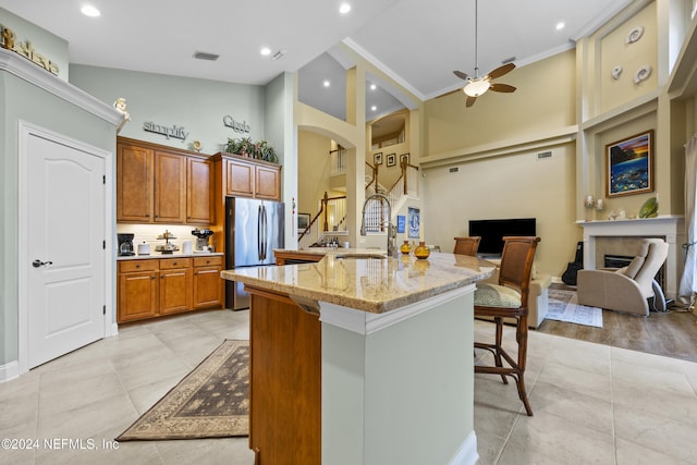 kitchen with a kitchen bar, stainless steel fridge, crown molding, high vaulted ceiling, and an island with sink