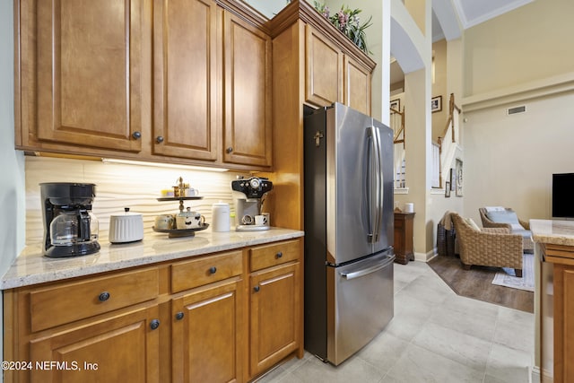 kitchen featuring light stone countertops, light wood-type flooring, tasteful backsplash, crown molding, and stainless steel refrigerator