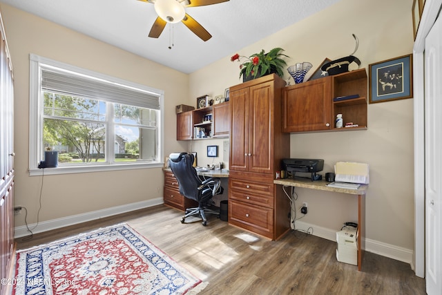 office featuring built in desk, ceiling fan, and dark wood-type flooring