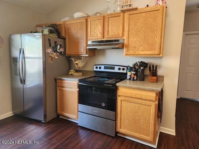 kitchen featuring a textured ceiling, stainless steel appliances, light brown cabinetry, and dark wood-type flooring