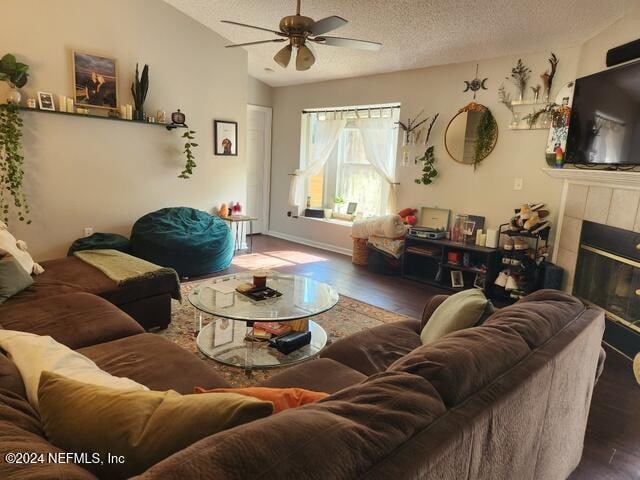 living room with a textured ceiling, a tiled fireplace, ceiling fan, and dark hardwood / wood-style floors