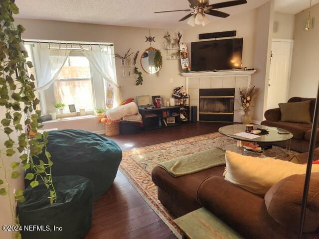 living room with ceiling fan, dark hardwood / wood-style flooring, a textured ceiling, and a tiled fireplace