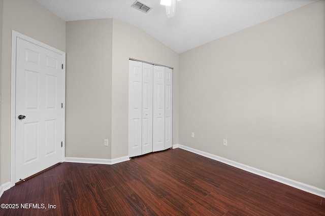 unfurnished bedroom with visible vents, a closet, baseboards, dark wood-style flooring, and vaulted ceiling