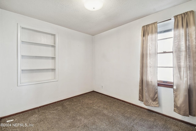 empty room featuring carpet, built in shelves, and a textured ceiling