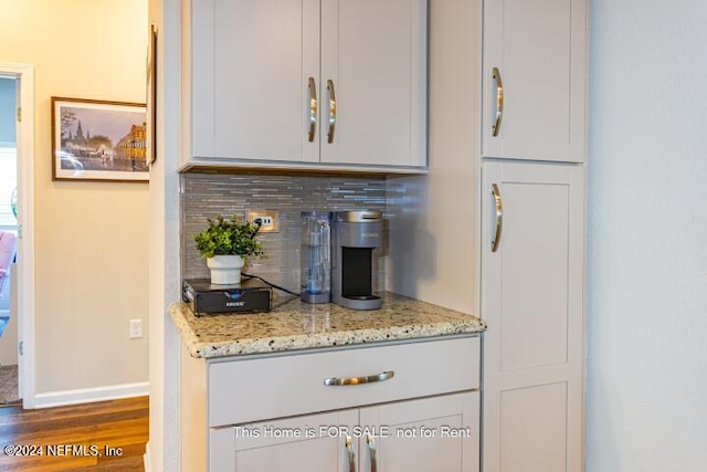 bar featuring white cabinets, tasteful backsplash, light stone counters, and dark hardwood / wood-style floors