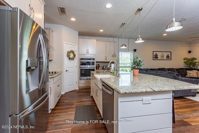 kitchen featuring white cabinetry, hanging light fixtures, an island with sink, a textured ceiling, and appliances with stainless steel finishes