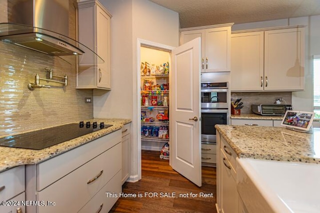 kitchen with wall chimney range hood, black electric cooktop, tasteful backsplash, dark hardwood / wood-style flooring, and stainless steel double oven