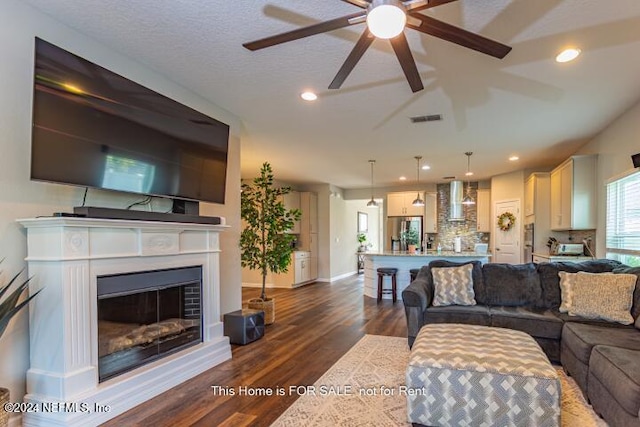 living room featuring ceiling fan, dark wood-type flooring, and a textured ceiling