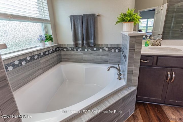 bathroom featuring hardwood / wood-style floors, vanity, and tiled bath