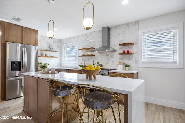 kitchen featuring plenty of natural light, light hardwood / wood-style floors, wall chimney range hood, and appliances with stainless steel finishes