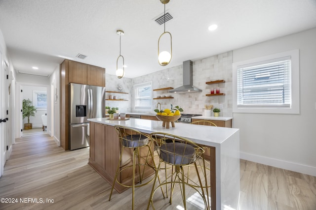 kitchen with appliances with stainless steel finishes, light wood-type flooring, wall chimney range hood, pendant lighting, and a center island