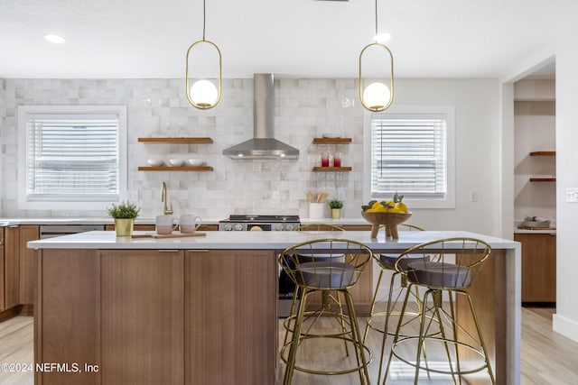 kitchen with wall chimney exhaust hood, a kitchen island, light wood-type flooring, and decorative light fixtures