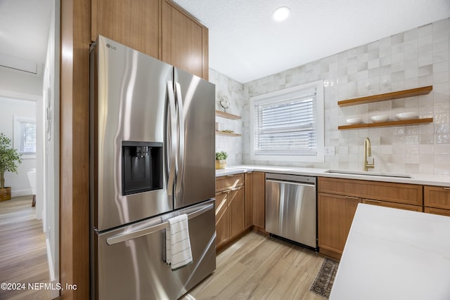 kitchen featuring sink, light wood-type flooring, tasteful backsplash, light stone counters, and stainless steel appliances