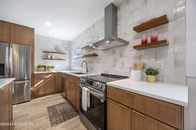 kitchen featuring wall chimney range hood, sink, decorative backsplash, light hardwood / wood-style floors, and stainless steel appliances