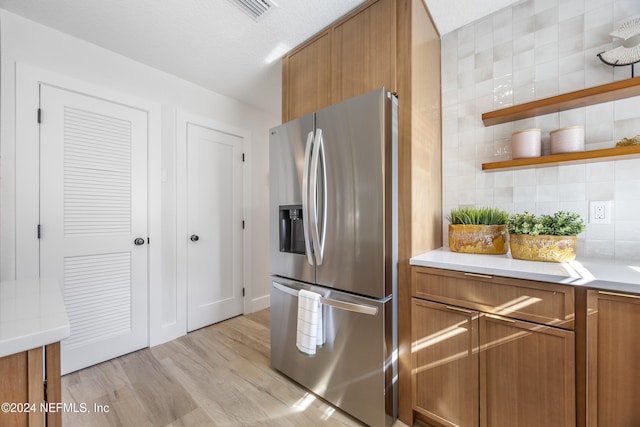 kitchen featuring stainless steel refrigerator with ice dispenser, light wood-type flooring, tasteful backsplash, and a textured ceiling