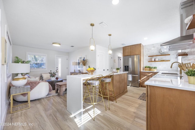 kitchen with pendant lighting, range hood, light hardwood / wood-style floors, stainless steel fridge with ice dispenser, and a breakfast bar area