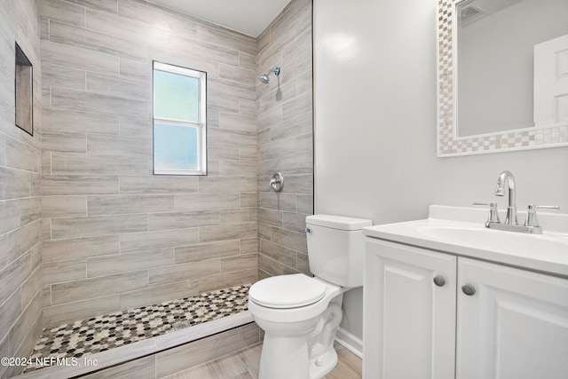 bathroom featuring a tile shower, vanity, and toilet