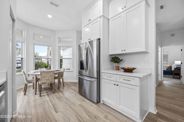 kitchen featuring stainless steel fridge, white cabinetry, a textured ceiling, and light hardwood / wood-style flooring