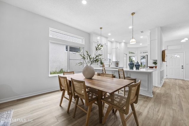 dining space with sink, a textured ceiling, and light wood-type flooring