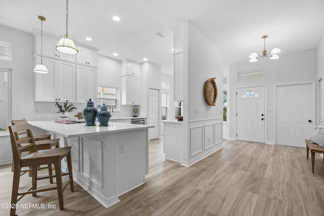 kitchen with kitchen peninsula, a textured ceiling, pendant lighting, white cabinetry, and a breakfast bar area