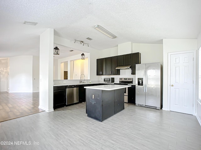 kitchen featuring light wood-type flooring, a textured ceiling, stainless steel appliances, sink, and a center island