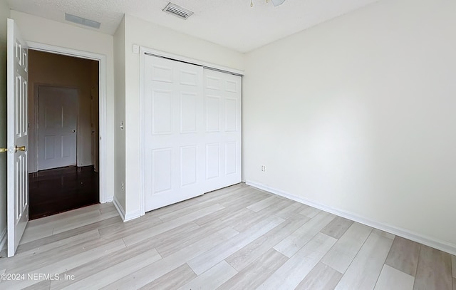 unfurnished bedroom with a textured ceiling, light hardwood / wood-style floors, and a closet