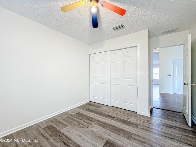 unfurnished bedroom with wood-type flooring, a textured ceiling, a closet, and ceiling fan