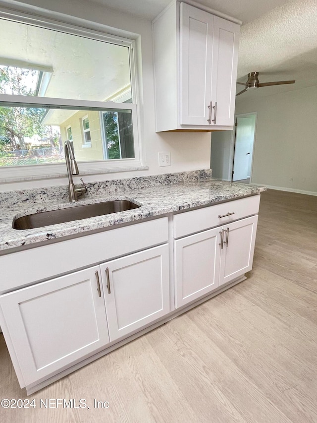 kitchen with light stone counters, ceiling fan, sink, light hardwood / wood-style flooring, and white cabinetry