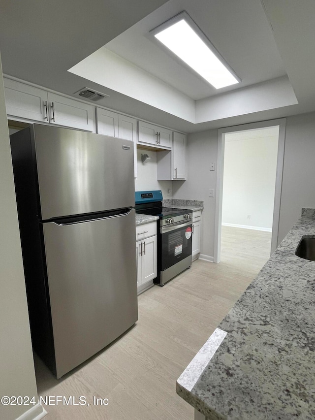 kitchen with light stone countertops, appliances with stainless steel finishes, a tray ceiling, white cabinets, and light wood-type flooring