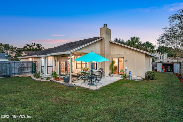 back house at dusk with a patio area and a lawn