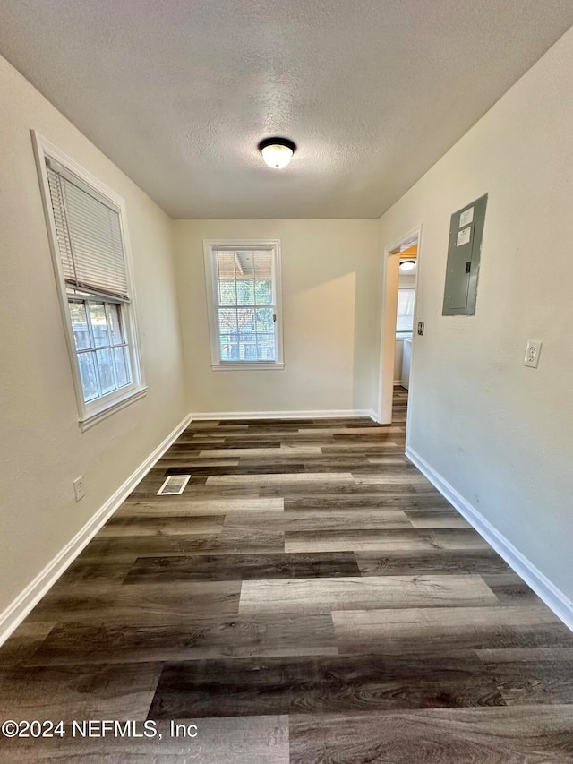 empty room with electric panel, baseboards, a textured ceiling, and wood finished floors