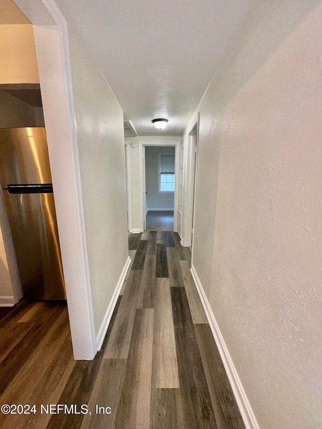 hall featuring dark wood-type flooring, baseboards, and a textured wall