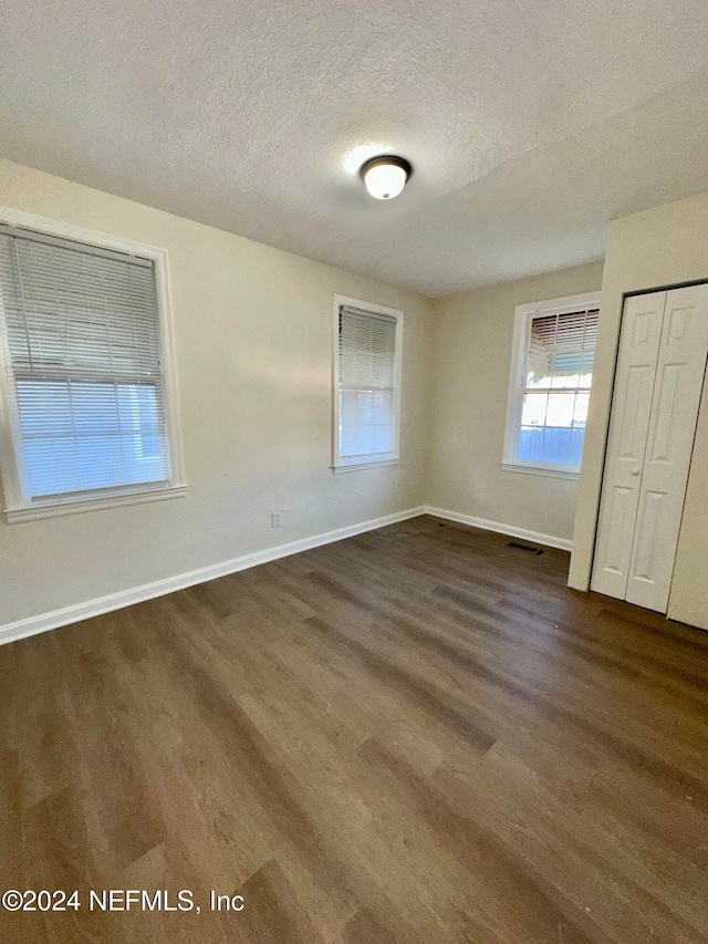 unfurnished bedroom featuring visible vents, baseboards, dark wood-type flooring, a closet, and a textured ceiling