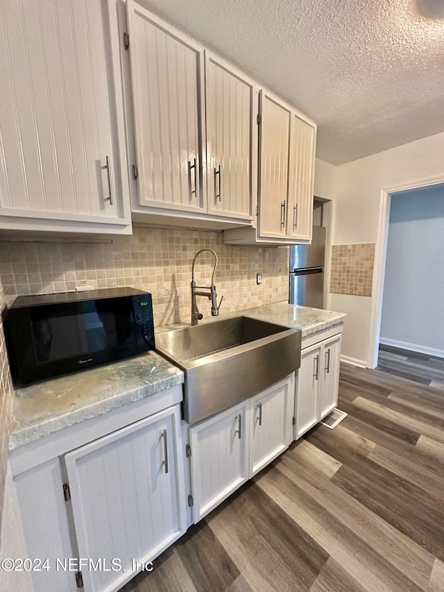 kitchen with dark wood-style flooring, freestanding refrigerator, a sink, black microwave, and a textured ceiling